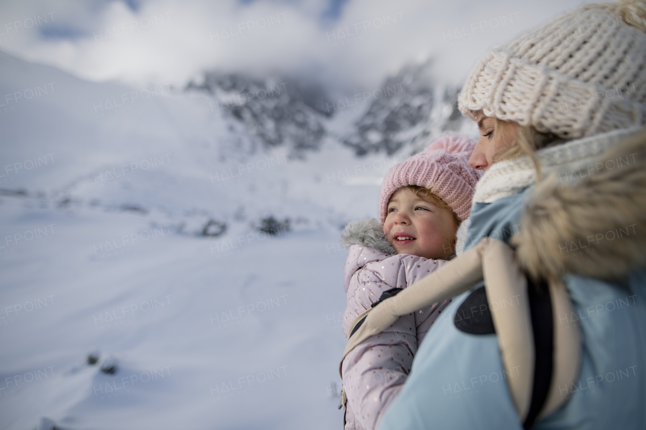 Mother standing in the middle of snowy landscape with daughter in baby carrier. Mom and girl enjoying winter holiday in mountains.