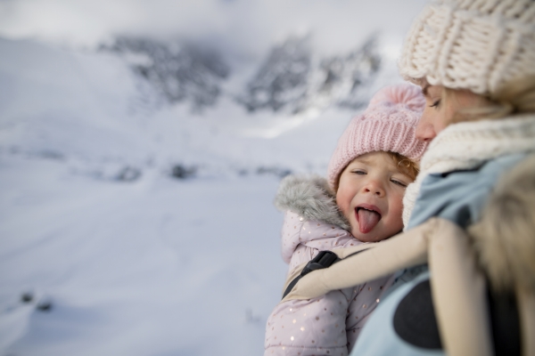 Mother standing in the middle of snowy landscape with daughter in baby carrier. Mom and girl enjoying winter holiday in mountains.