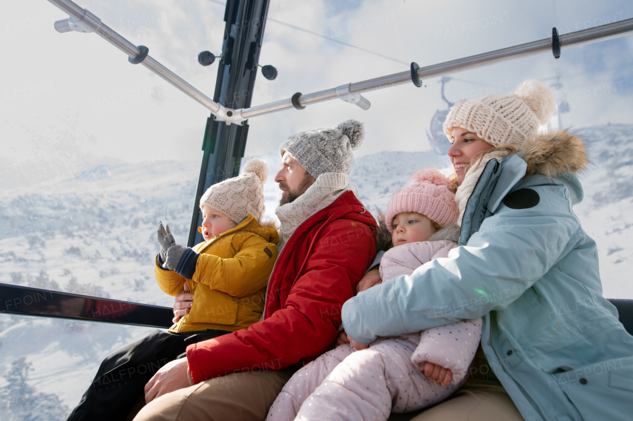 Young family on a winter holiday is riding a cable car to the top of the hill or mountain.