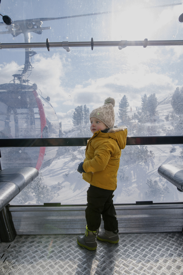 Little boy riding cable car to the top of the mountain during winter holiday with his family