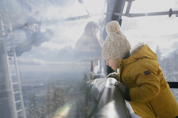 Little boy riding cable car to the top of the mountain during winter holiday with his family