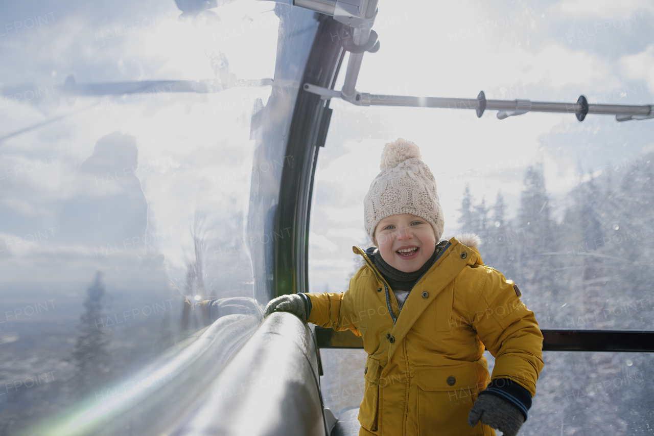 Little boy riding cable car to the top of the mountain during winter holiday with his family