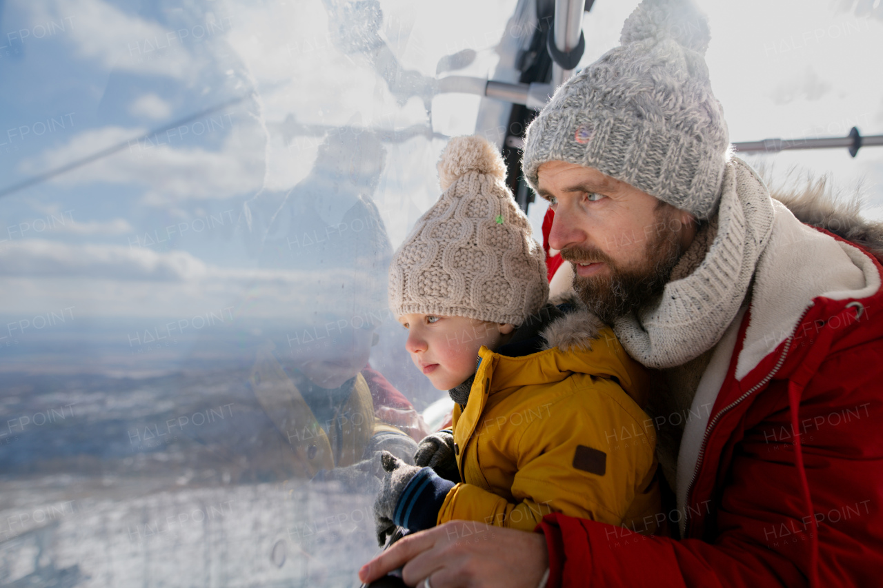 Father and young son on a winter holiday is riding cable car to the top of the hill or mountain.