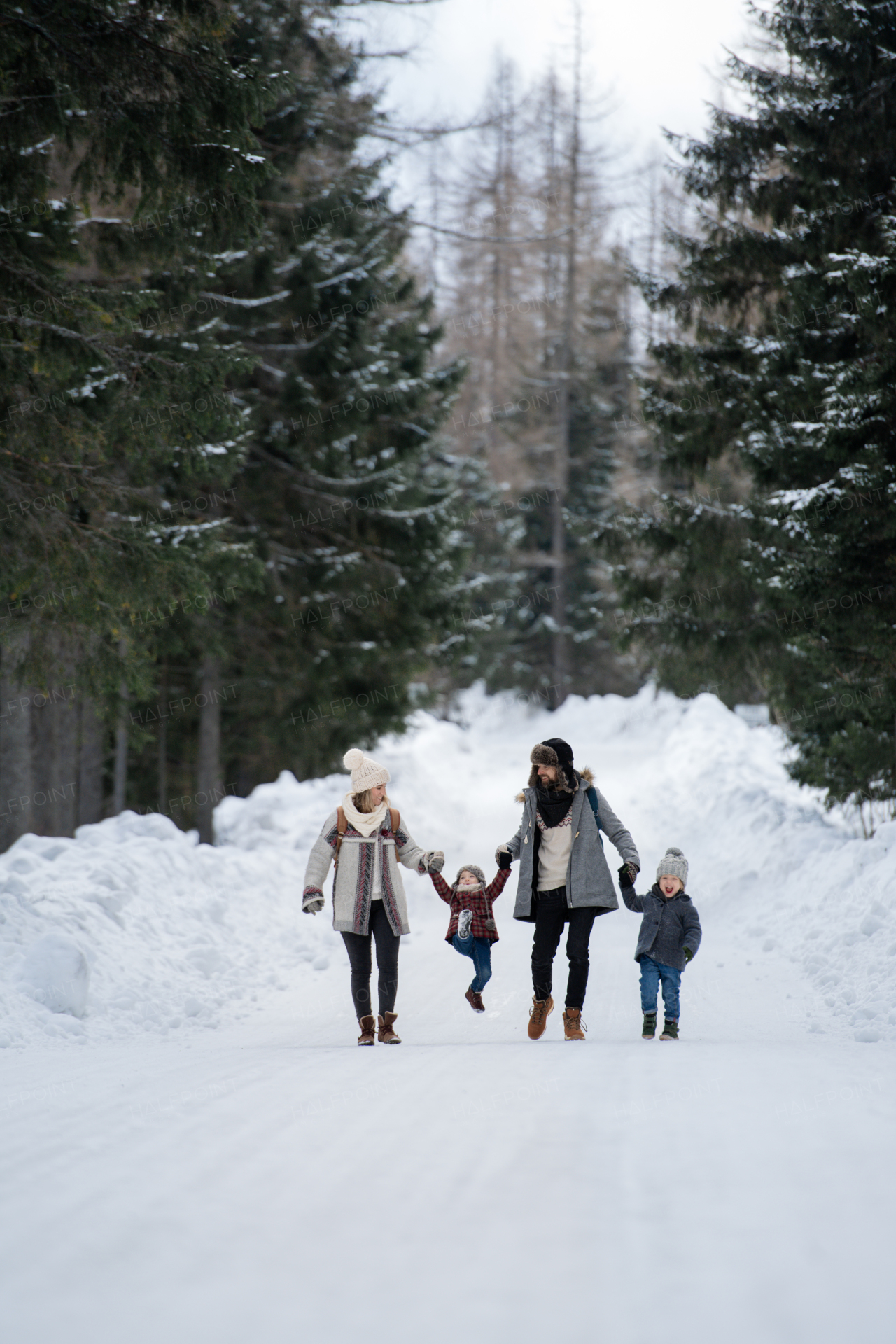 Family is enjoying winter holiday in the mountains, holding hands while walking through the snowy forest.