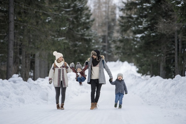 Family is enjoying winter holiday in the mountains, holding hands while walking through the snowy forest.