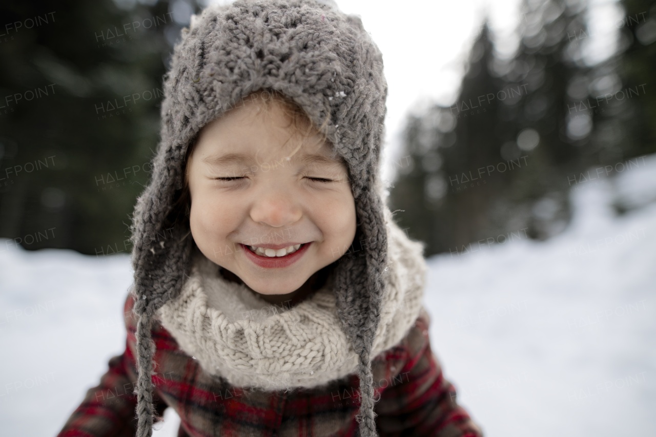 Portrait of a small girl with closed eyes enjoying winter holiday in the mountains with family, playing in snow.