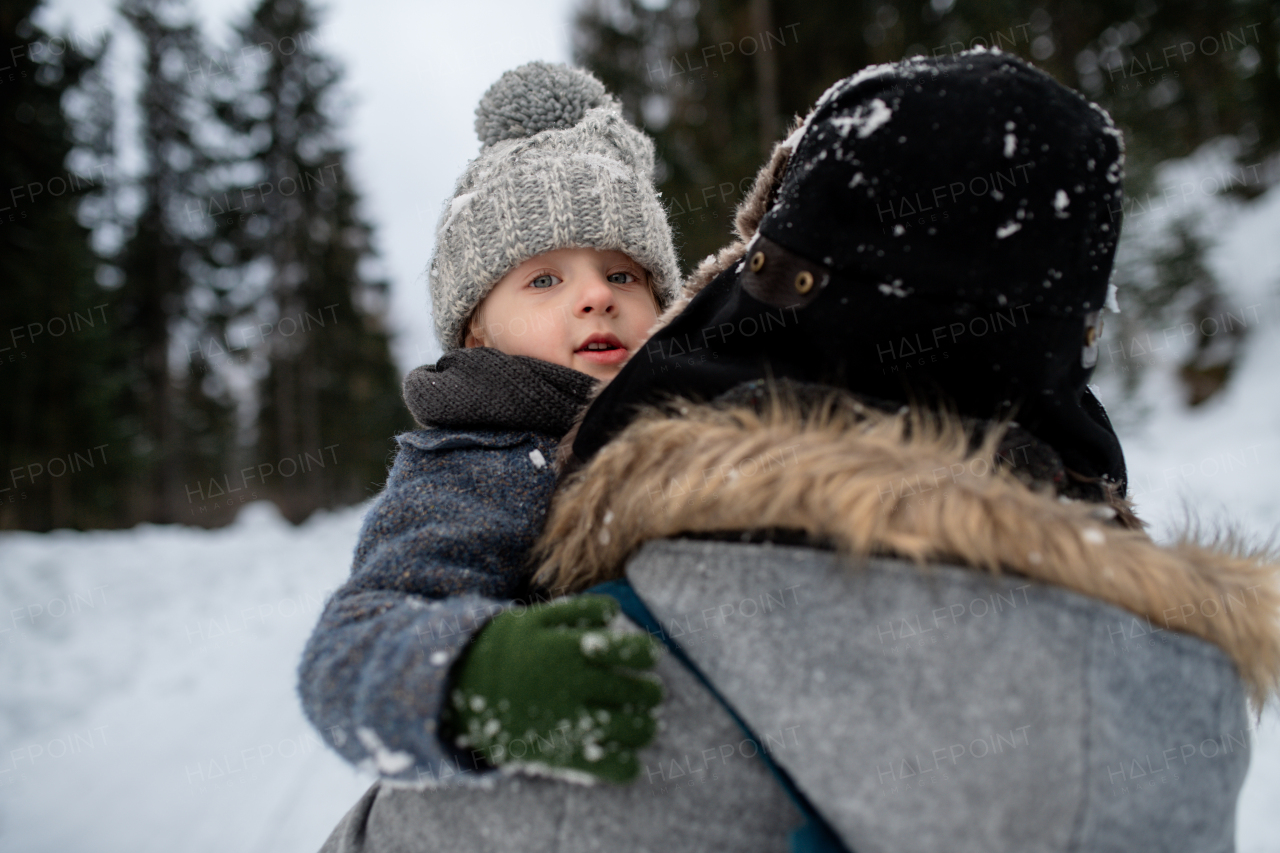 Father standing in the middle of snowy forest holding young son in arms. Dad and boy enjoying winter holiday in the mountains