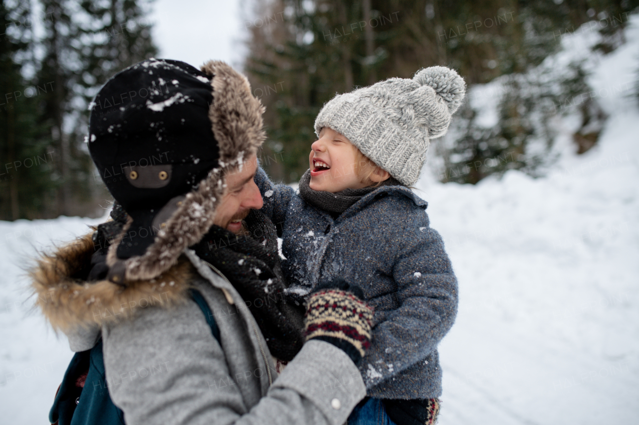 Father standing in the middle of snowy forest holding young son in arms. Dad and boy enjoying winter holiday in the mountains