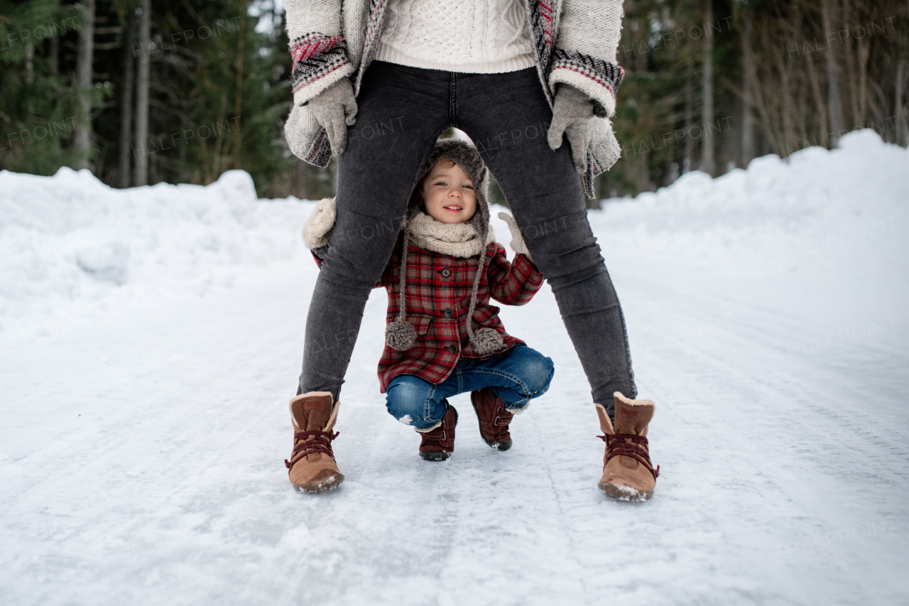 Girl crouching between her mothers legs, looking at the camera. Mom and girl enjoying winter holiday in mountains.