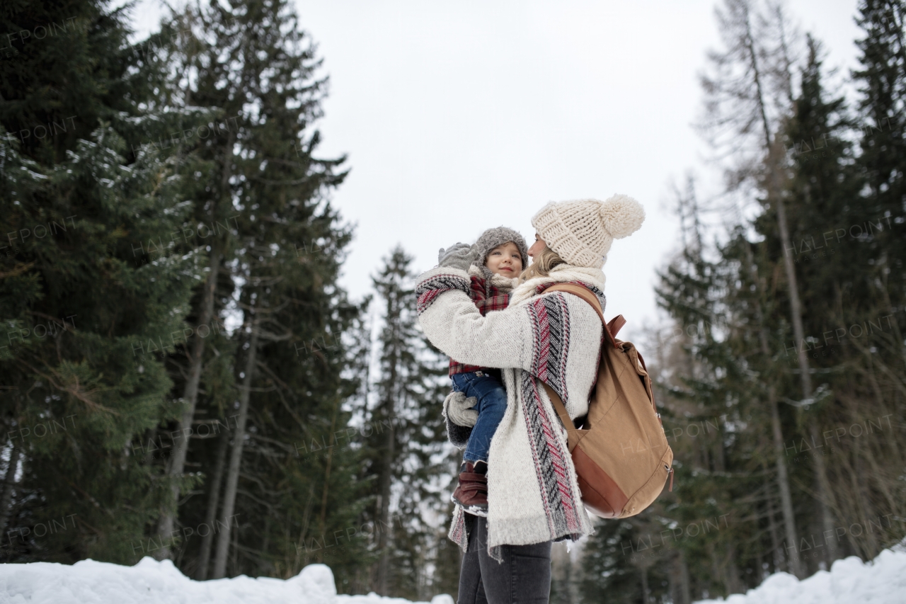 Mother standing in the middle of snowy landscape holding daughter in arms. Mom and girl enjoying winter holiday in the mountains