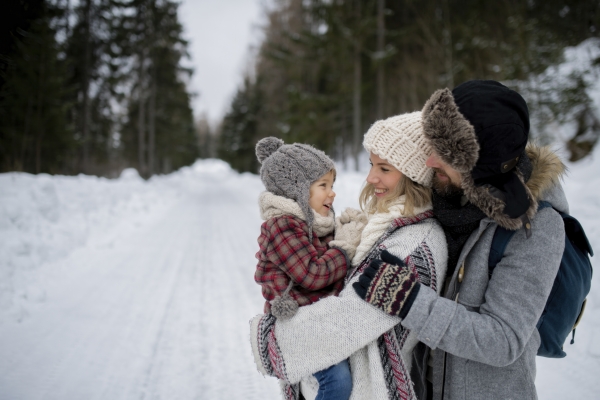 Family is enjoying winter holiday in the mountains, standing in the middle of snowy forest.