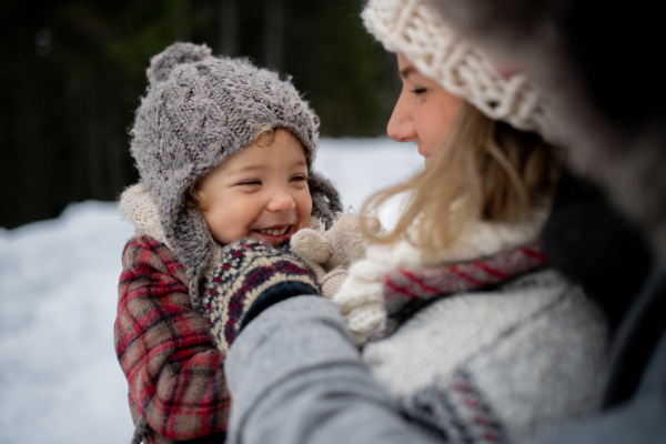 Mother standing in the middle of snowy landscape holding daughter in arms. Mom and girl enjoying winter holiday in the mountains