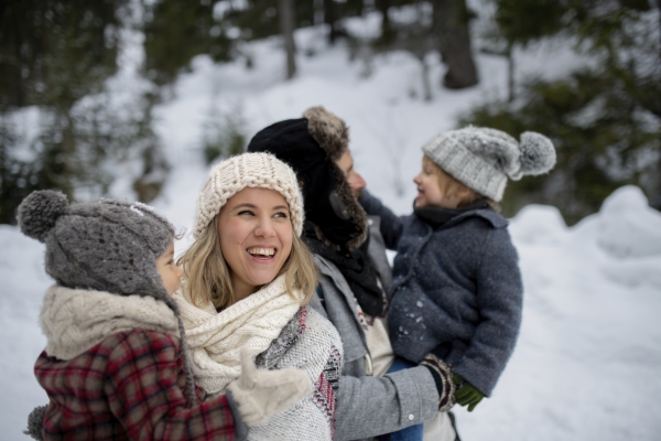 Family is enjoying winter holiday in the mountains, standing in the middle of snowy forest.