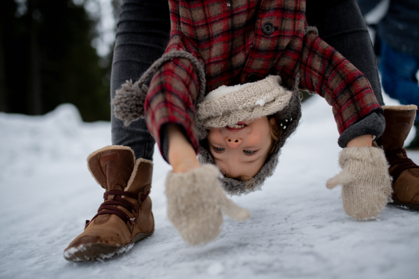 Girl is upside down, mother holding her by legs. Mom and girl enjoying winter holiday in mountains.