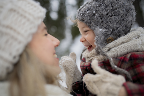 Mother standing in the middle of snowy landscape holding daughter in arms. Mom and girl enjoying winter holiday in the mountains