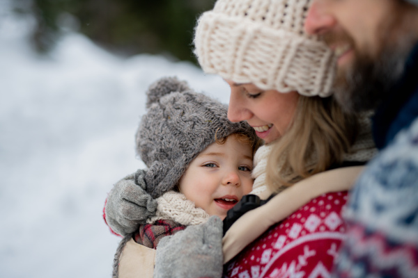 Mother and father standing in the middle of snowy landscape with daughter in baby carrier. Mom and girl enjoying winter holiday in mountains.