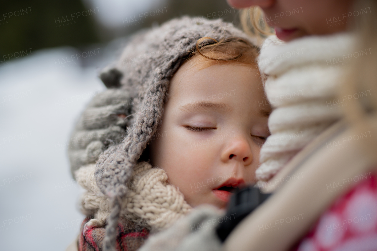 Mother standing in the middle of snowy landscape with sleeping daughter in baby carrier. Mom and girl enjoying winter holiday in mountains.