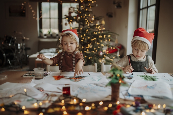 Siblings making holiday Christmas cards for family. Children painting pictures for Santa Claus, making christmas decorations with watercolors.