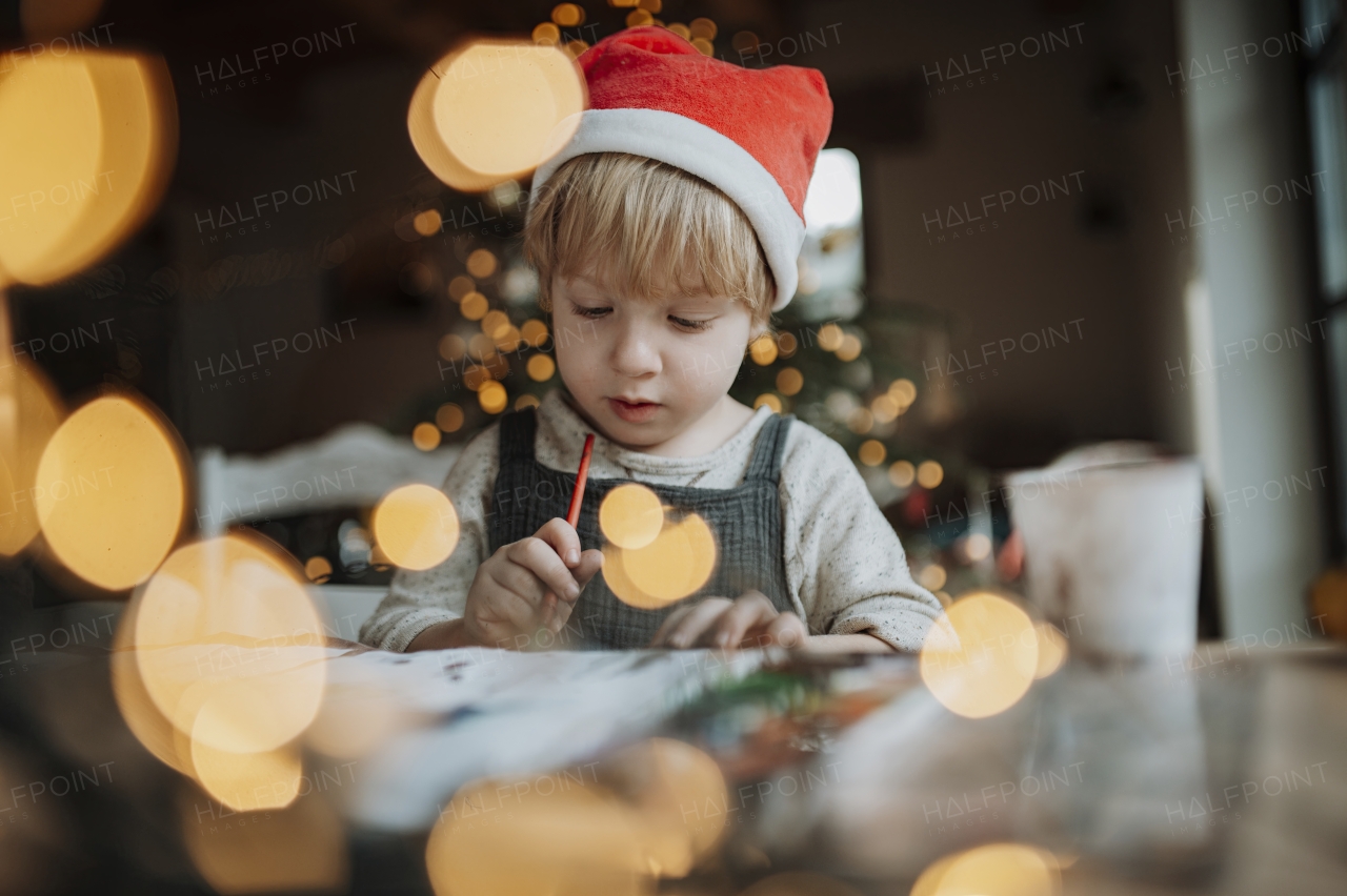 Portrait of young boy at Christmas home, painting picture for Santa Claus or making christmas decoration. Santa's hat on head.