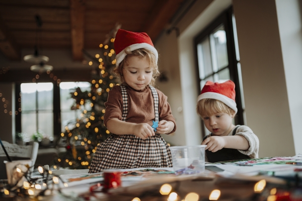 Siblings making holiday Christmas cards for family. Children painting pictures for Santa Claus, making christmas decorations with watercolors.