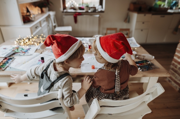 Rear view of siblings making holiday Christmas or a christmas decorations at home. Creative activity for toddlers.