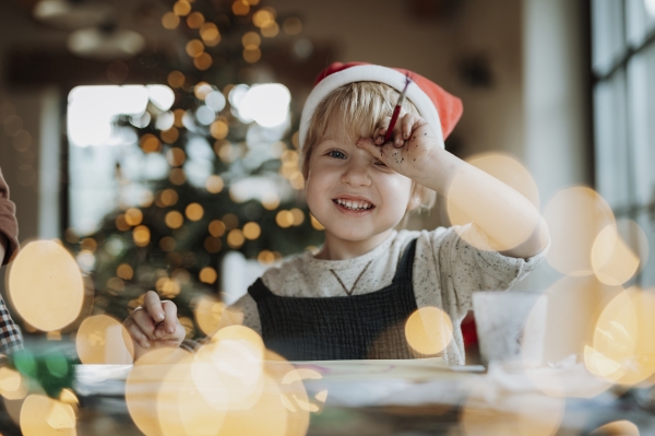 Portrait of young boy at Christmas home, painting picture for Santa Claus or making christmas decoration. Santa's hat on head.