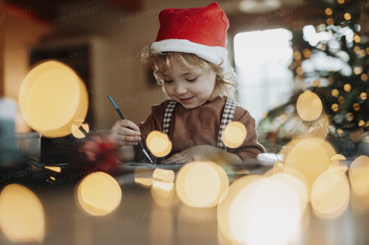 Portrait of small girl indoors at Christmas home, painting picture for Santa Claus or making christmas decoration.