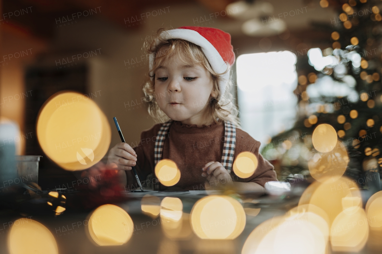 Portrait of small girl indoors at Christmas home, painting picture for Santa Claus or making christmas decoration.