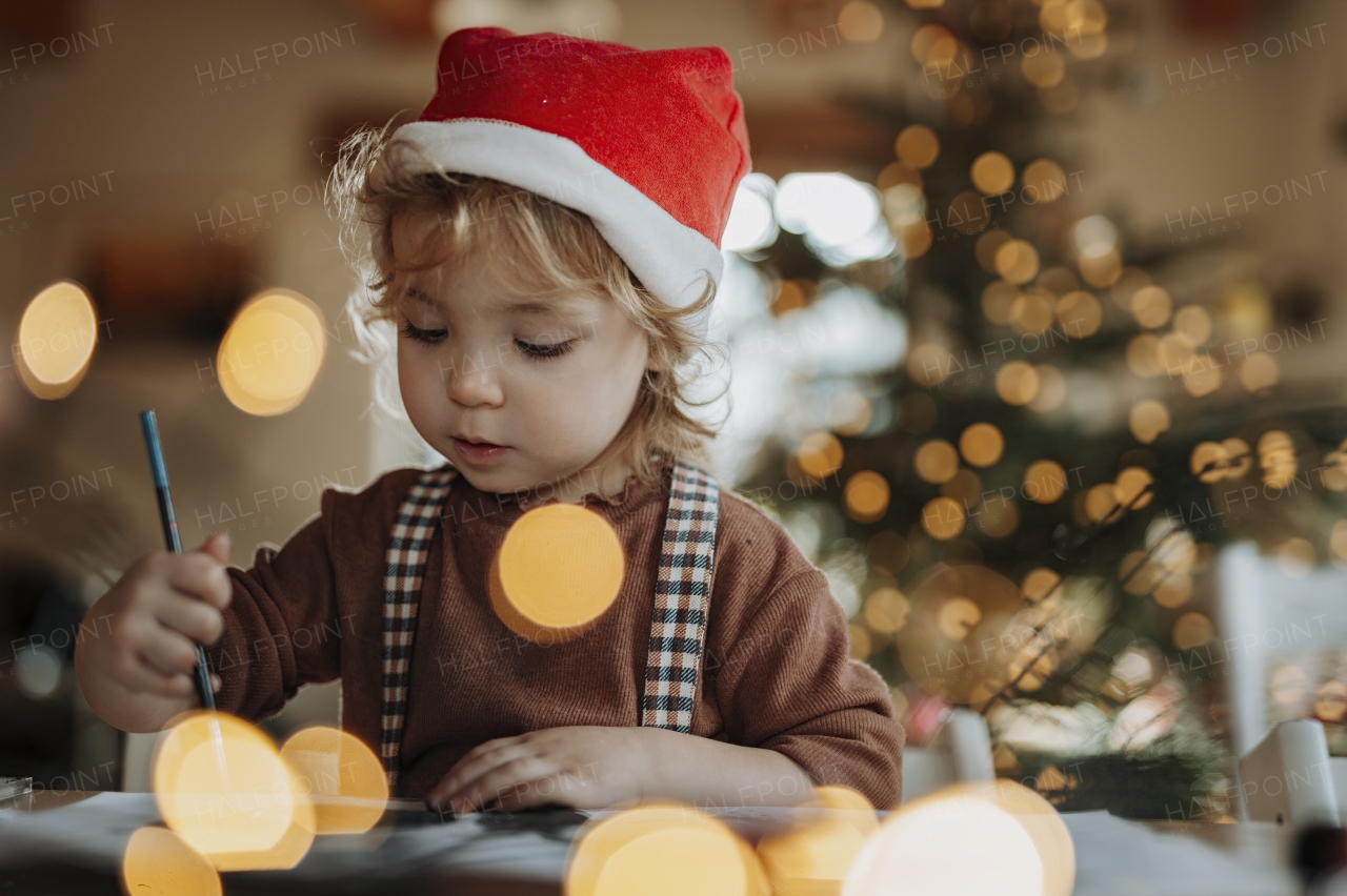 Portrait of small girl indoors at Christmas home, painting picture for Santa Claus or making christmas decoration.