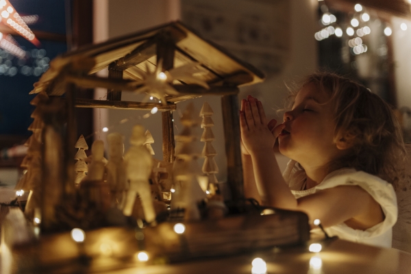 Cute girl praying at the Christmas nativity scene or Christmas crib with closed eyes and hands folded in prayer