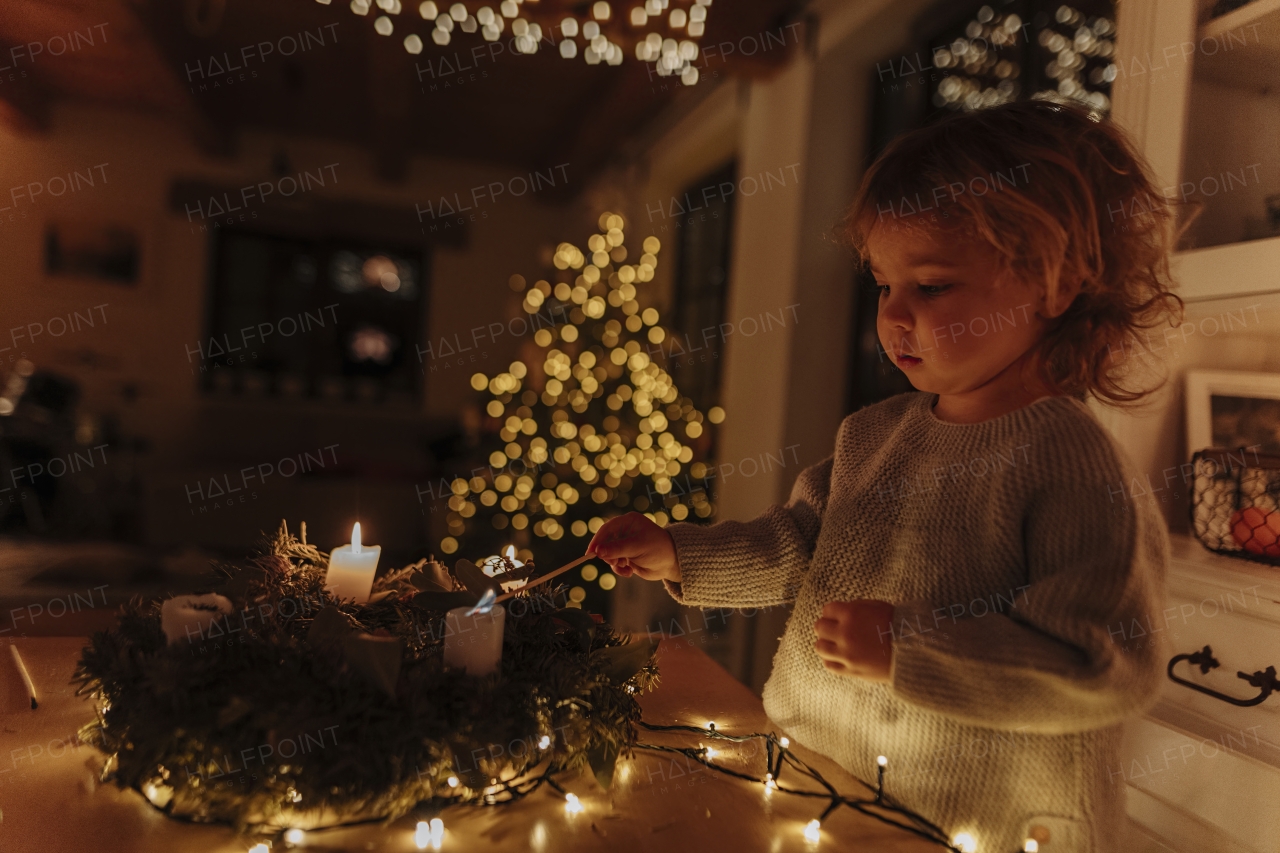 Little girl lighting candles on advent wreath. Christian traditon.