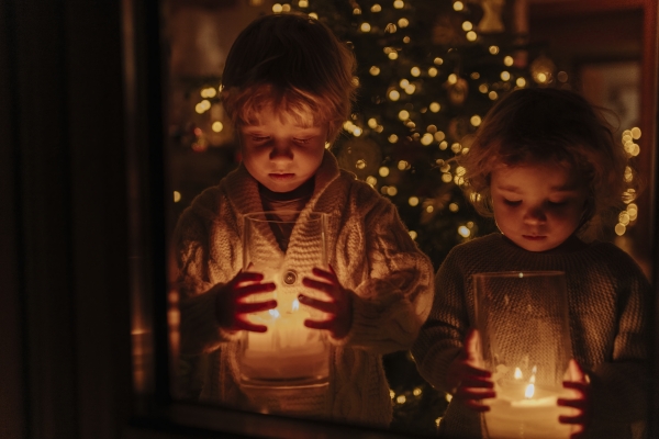 Cute siblings holding Christmas candles in their hands, Christmas tree behind them. Festive christmas atmosphere at home.