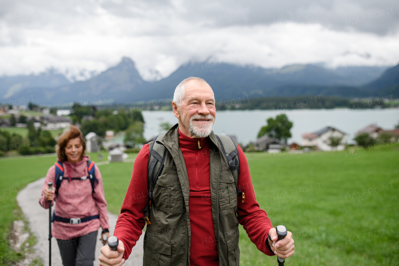 Portrait of active elderly couple hiking together in mountains. Senior tourists walking with trekking poles for stability.