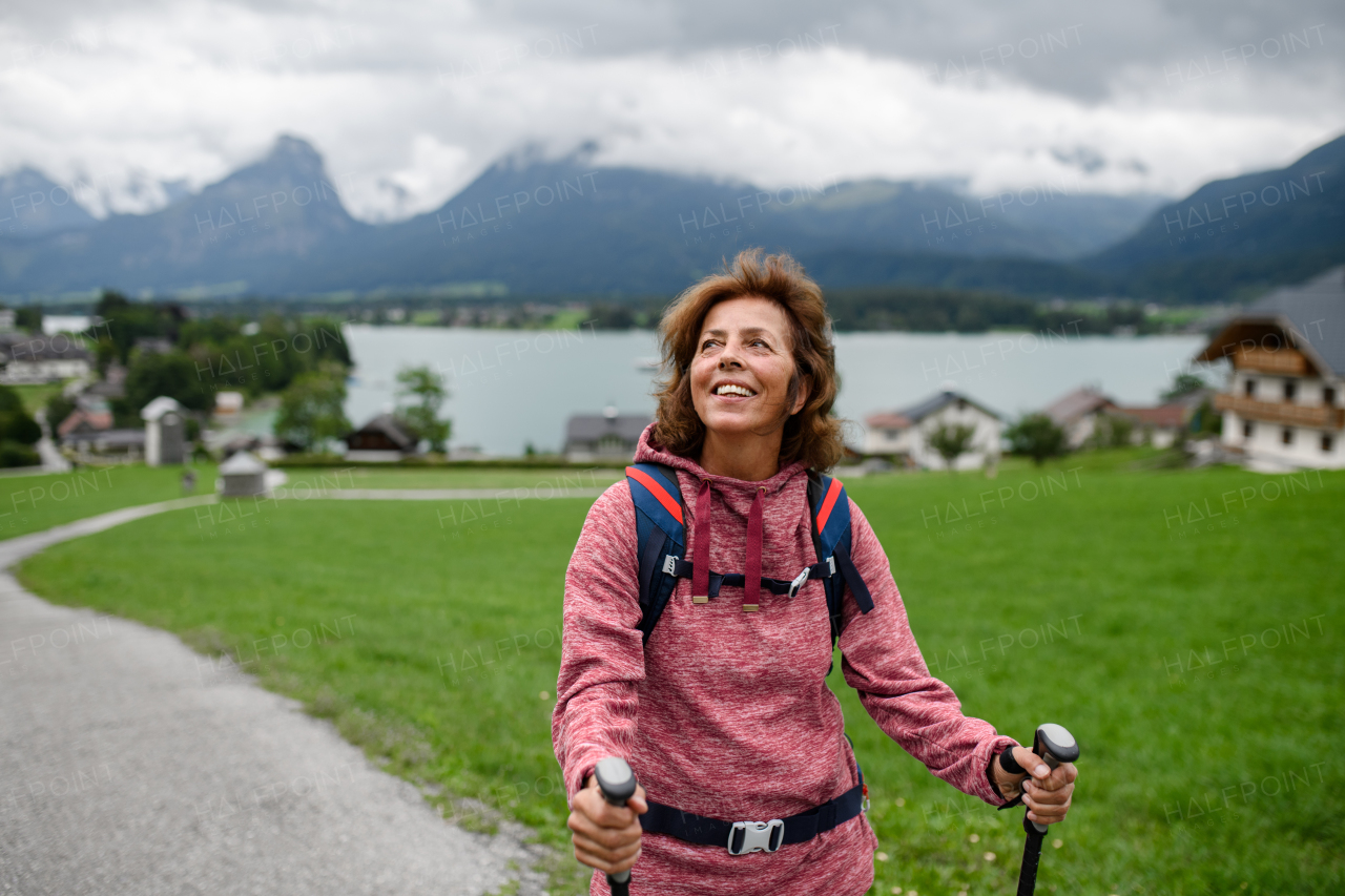 Portrait of beautiful elderly woman walking outdoors with trekking poles, going on hiking trail. Senior tourists enjoying view.