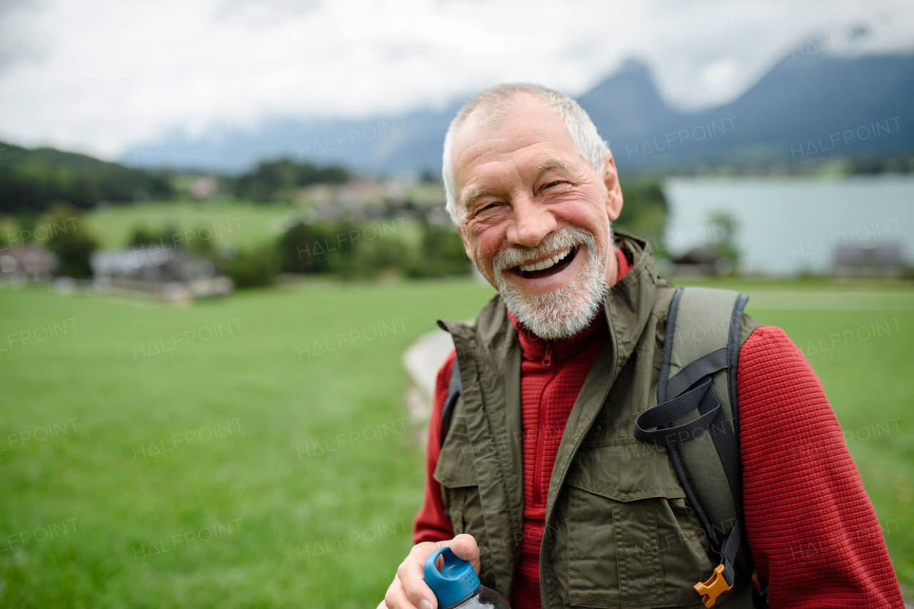 Portrait of smiling elderly man walking outdoors with trekking poles, going on hiking trail. Senior tourists enjoying view.