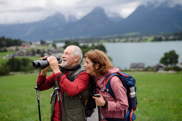 Active elderly couple hiking together in autumn mountains. Senior tourists enjoying nature look through a binoculars.