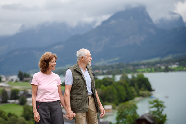 Active elderly couple hiking together in spring mountains. Senior tourists enjoying nature and exercising.