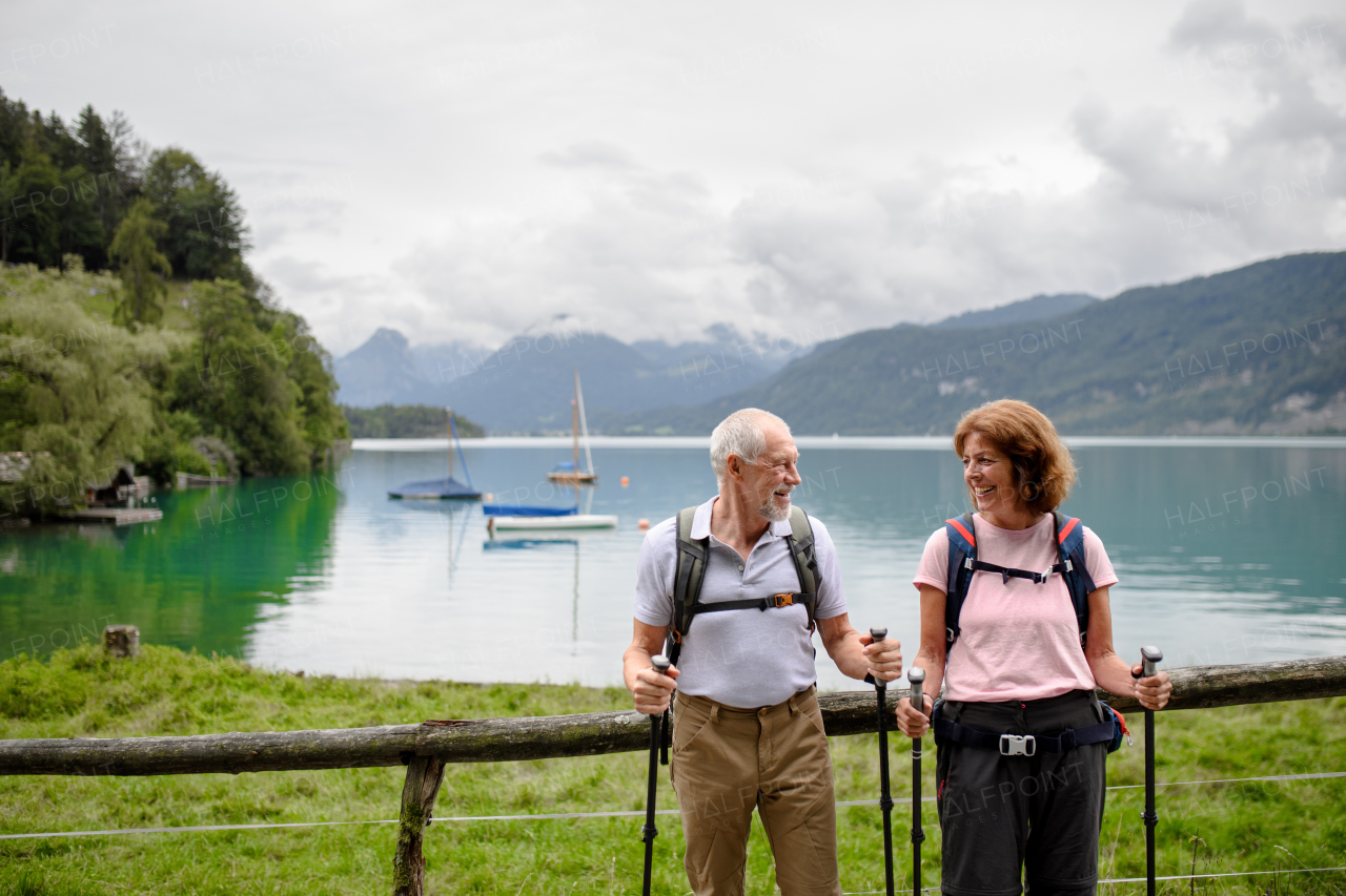 Portrait of active elderly couple hiking together in mountains. Senior tourists walking with trekking poles for stability.