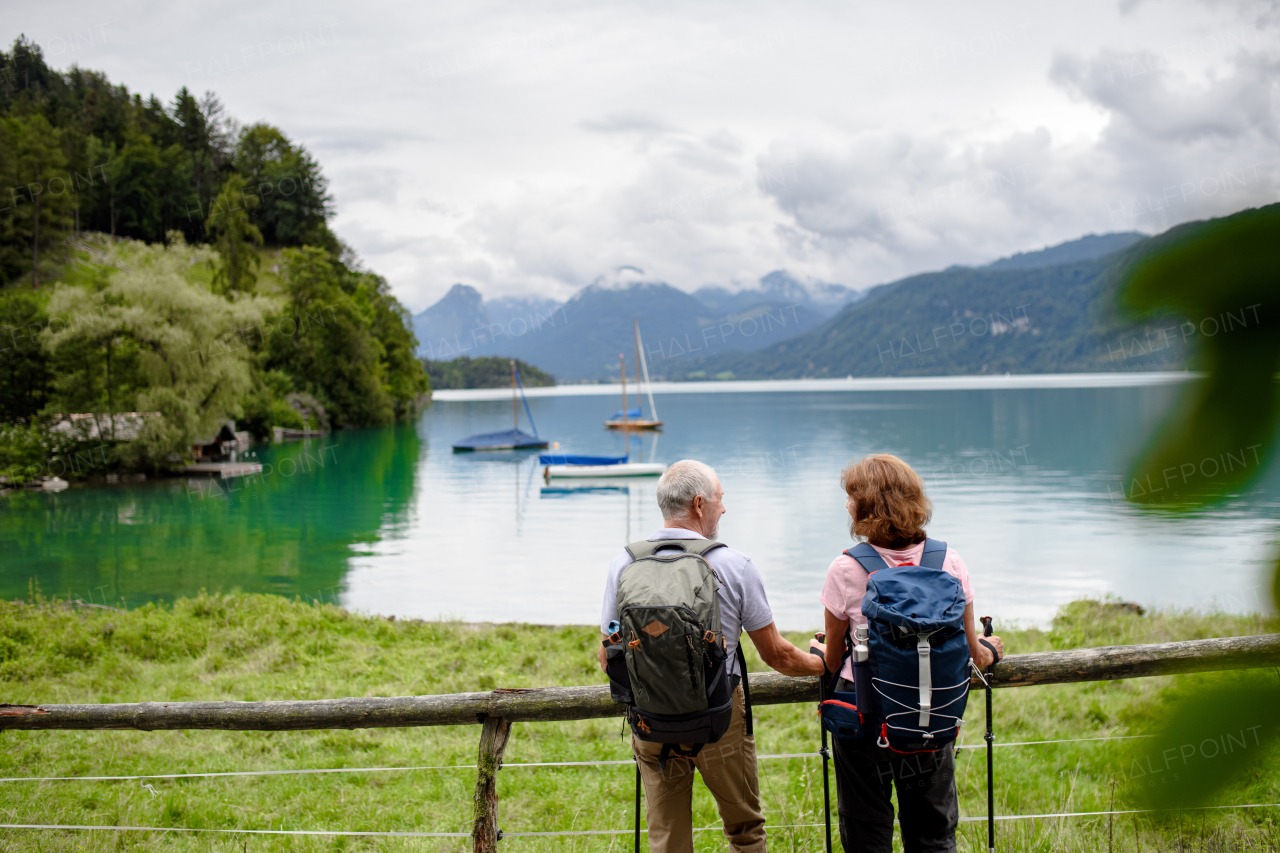 Rear view of beautiful active elderly couple hiking together in autumn mountains. Senior tourists looking at a lake.