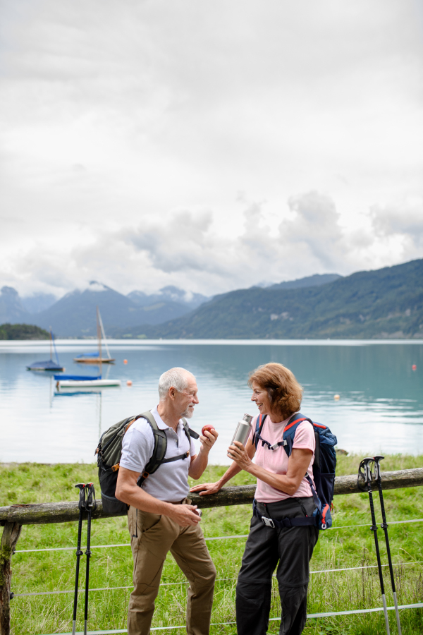 Active elderly couple hiking together in a mountains. Drinking coffee and having healthy snack, to get energy. Senior tourist with backpacks resting during hike.