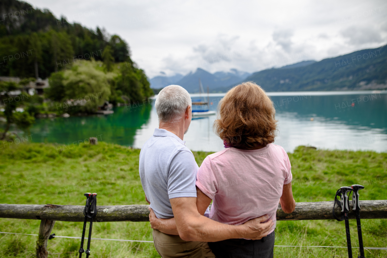 Rear view of beautiful active elderly couple hiking together in autumn mountains. Senior tourists looking at a lake.