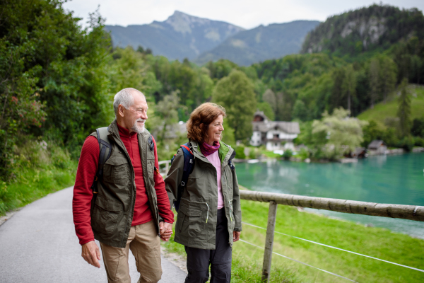 Active elderly couple hiking together in autumn mountains and holding hands. Senior tourists enjoying view on lake.