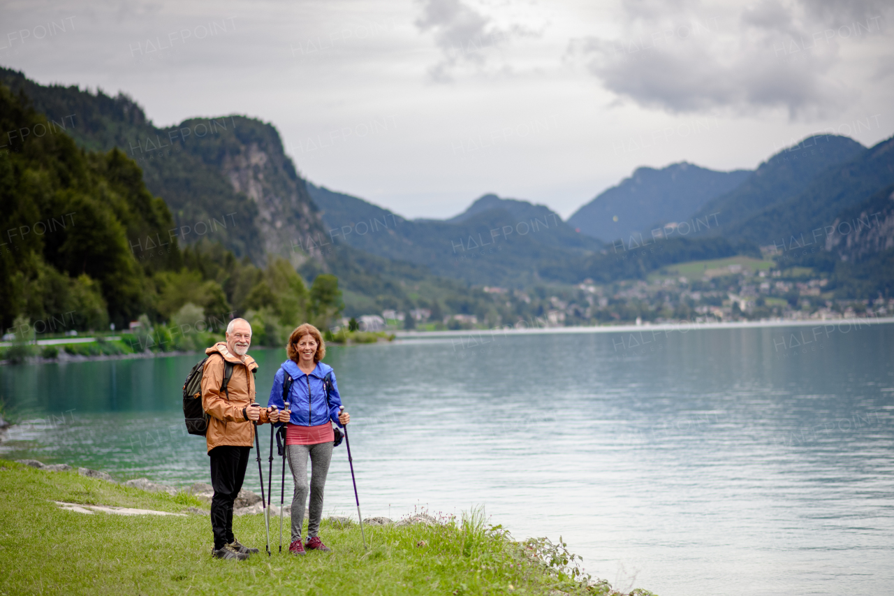 Portrait of beautiful active elderly couple hiking together in spring mountains. Senior tourists embracing each other in front of a lake.