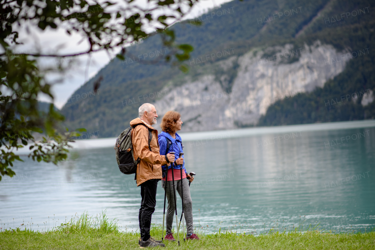 Portrait of beautiful active elderly couple hiking together in autumn mountains. Senior tourists looking at a lake.