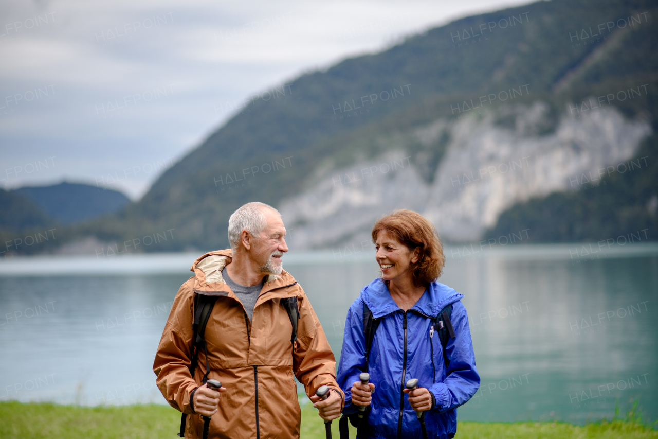 Portrait of beautiful active elderly couple hiking together in spring mountains. Senior tourists standing in front of a lake.