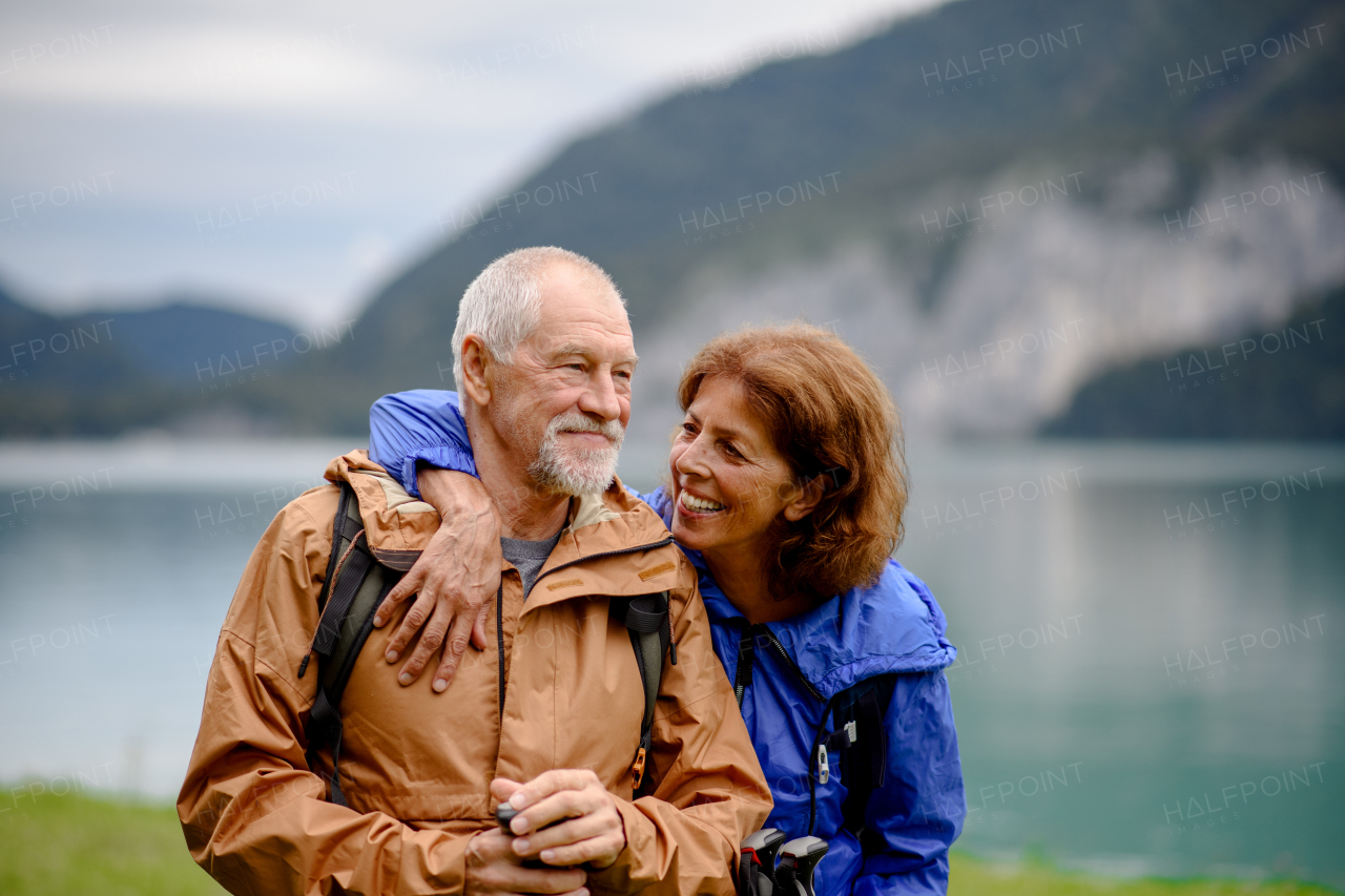 Portrait of beautiful active elderly couple hiking together in autumn mountains. Senior tourists embracing each other in front of a lake.