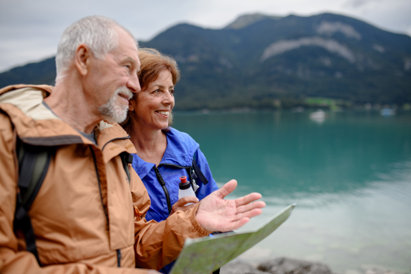 Portrait of beautiful active elderly couple hiking together in spring mountains. Senior tourists looking at map in front of a lake.