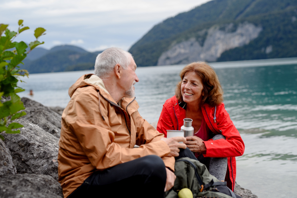 Active elderly couple hiking together in a mountains. Drinking coffee and having healthy snack, to get energy. Senior tourist with backpacks resting during hike.