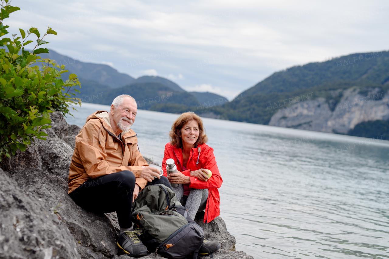 Active elderly couple hiking together in a mountains. Drinking coffee and having healthy snack, to get energy. Senior tourist with backpacks resting during hike.