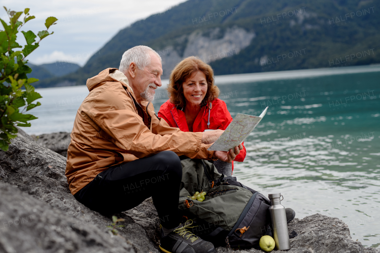 Active elderly couple hiking together in mountains, checking trail in map. Drinking coffee and having healthy snack, to get energy. Senior tourist with backpacks resting during hike.